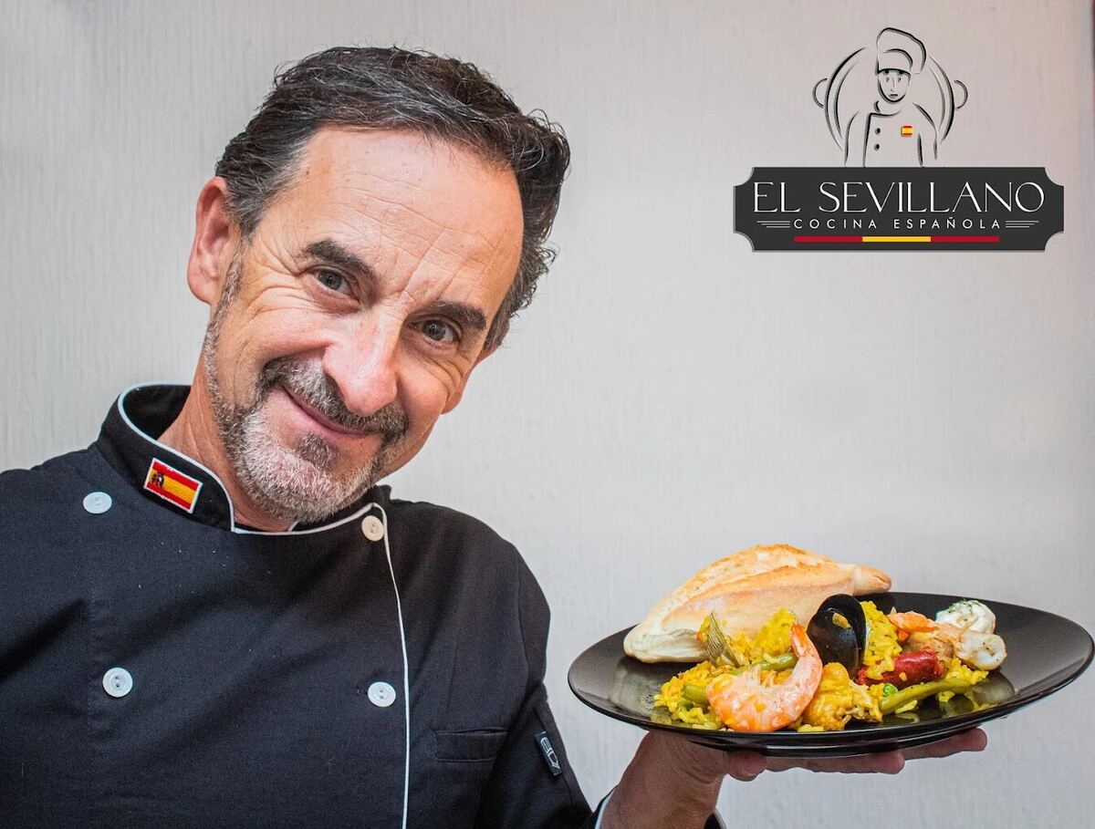 Chef de El Sevillano sosteniendo un plato de paella junto al logo